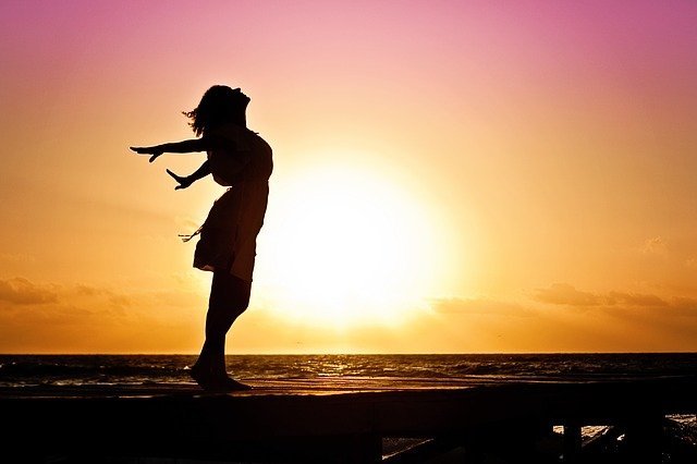 夕日が落ちる海辺に立つ女性